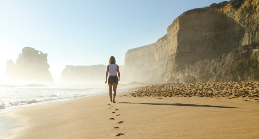 Woman walks on beach with cliffs nearby