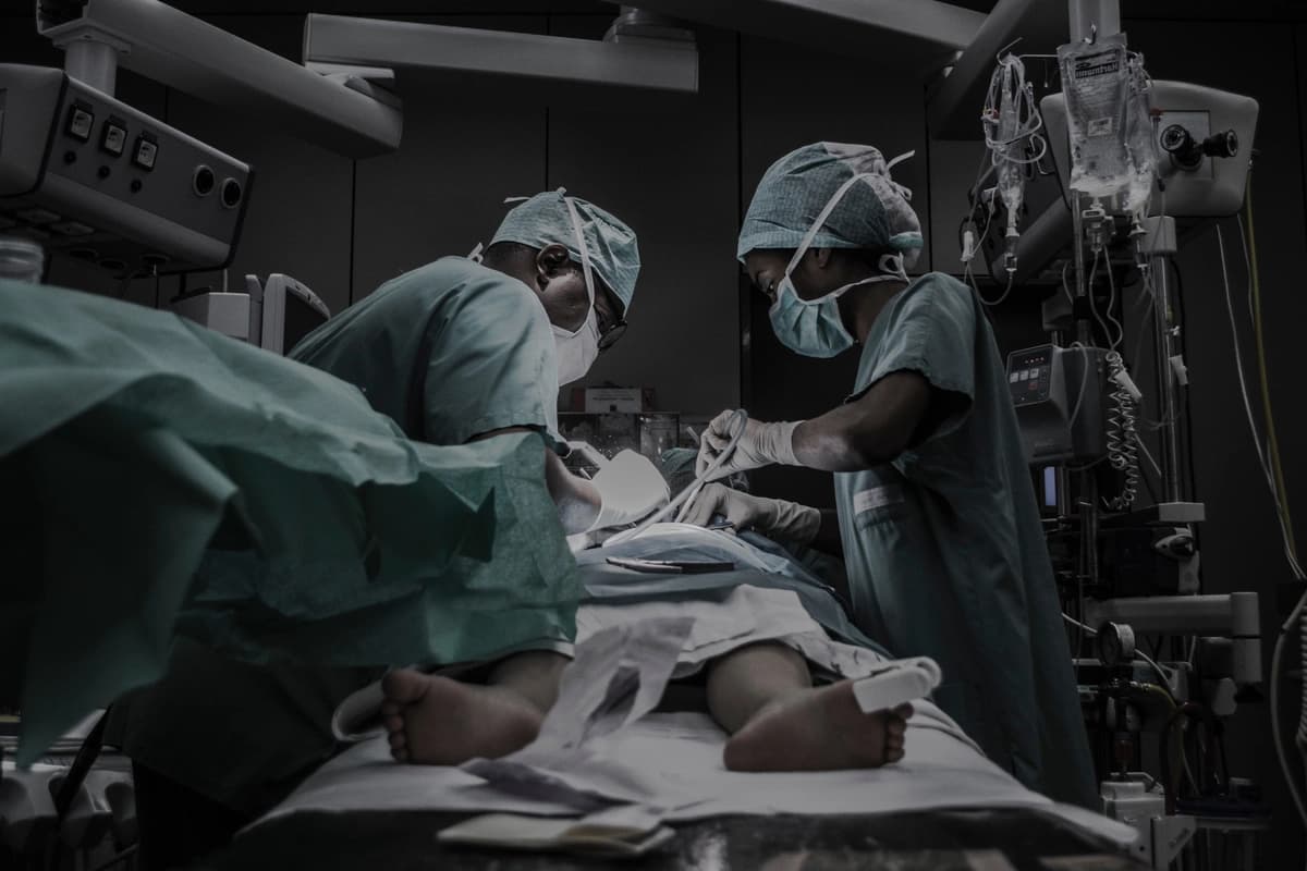 Two surgeons lean over patient, doing abdominal surgery