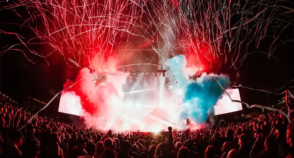 Crowd at a concert with stage lit up in bright red, blue, and white lights