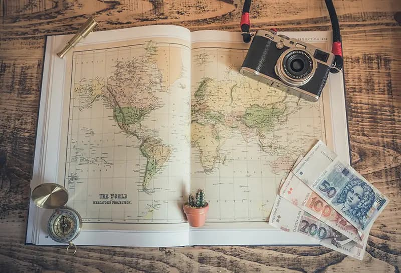 Atlas laying on a table with a camera, compass, and international currency