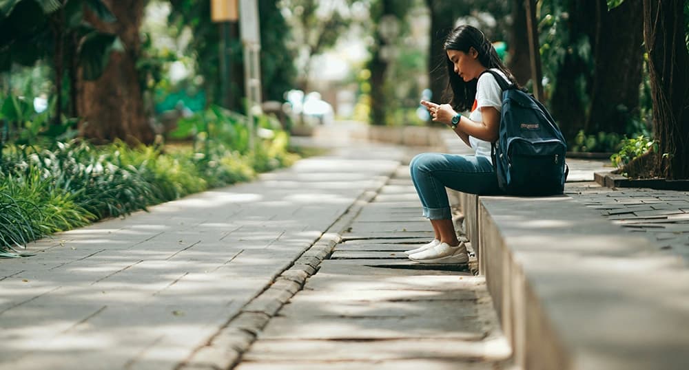 Young woman sitting on stone bench, looking at phone