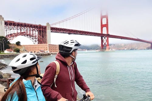 Young couple on guided bicycle sight seeing tour looking at Golden Gate Bridge.