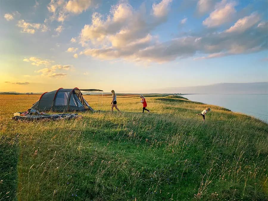 Three people camping in a tent along the water