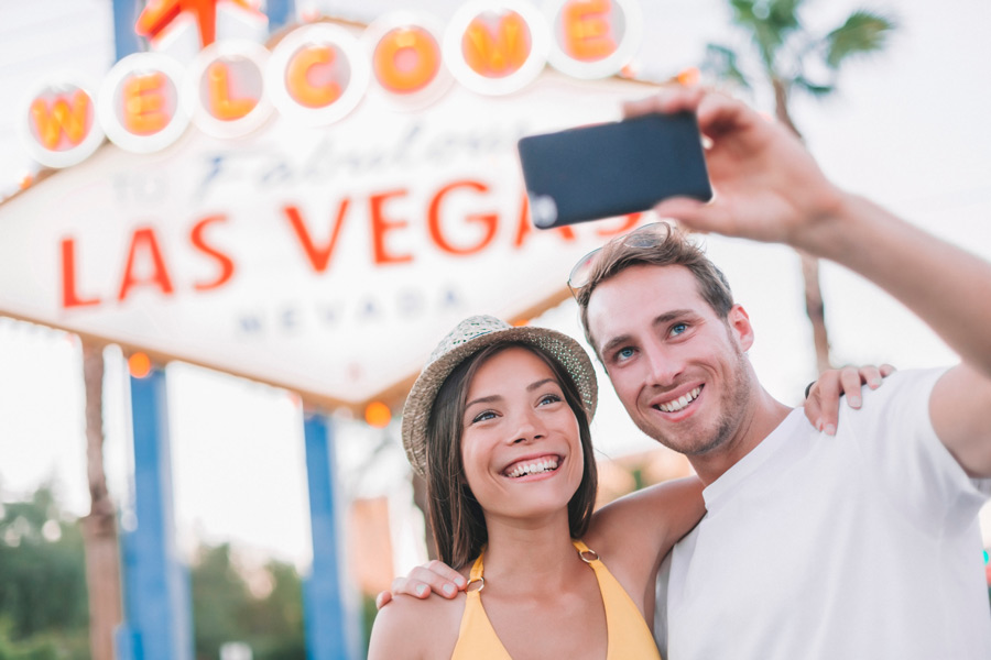 Tourist couple smiles and takes cell phone photo in front of Las Vegas sign